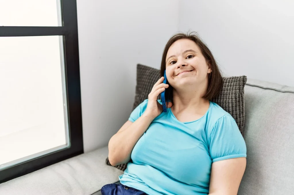 Happy disabled woman with down syndrome sitting on couch making phone call