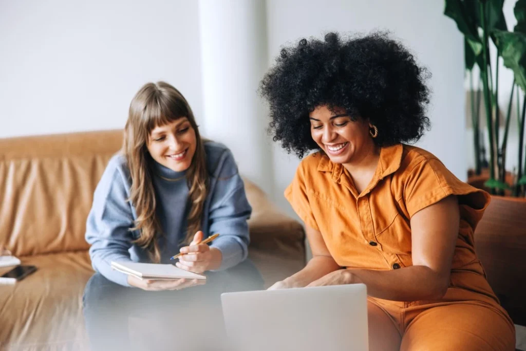 Two happy women sitting in office looking at laptop