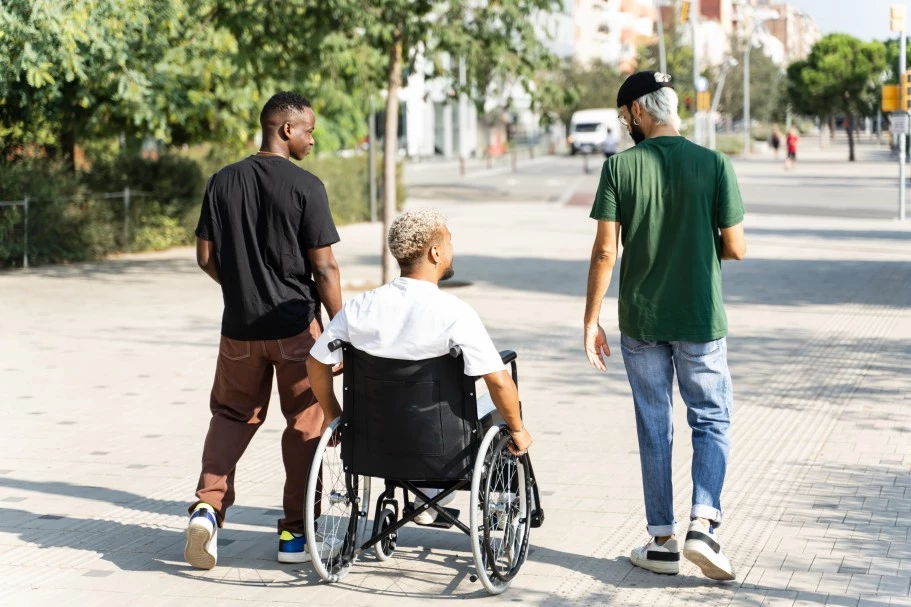 Disabled man in wheelchair outdoors with two friends